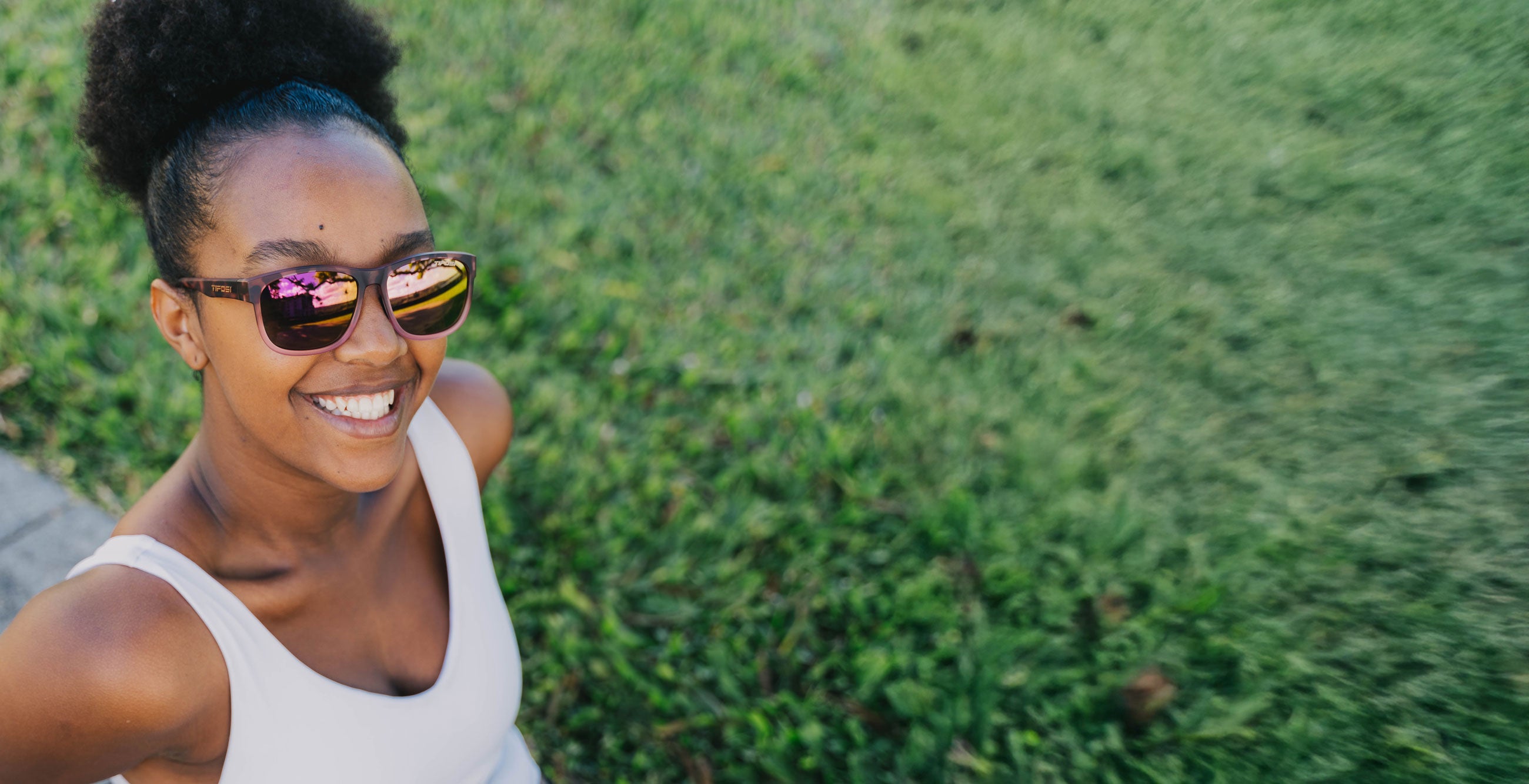 Woman standing outside by grass wearing pink tortoise sunglasses