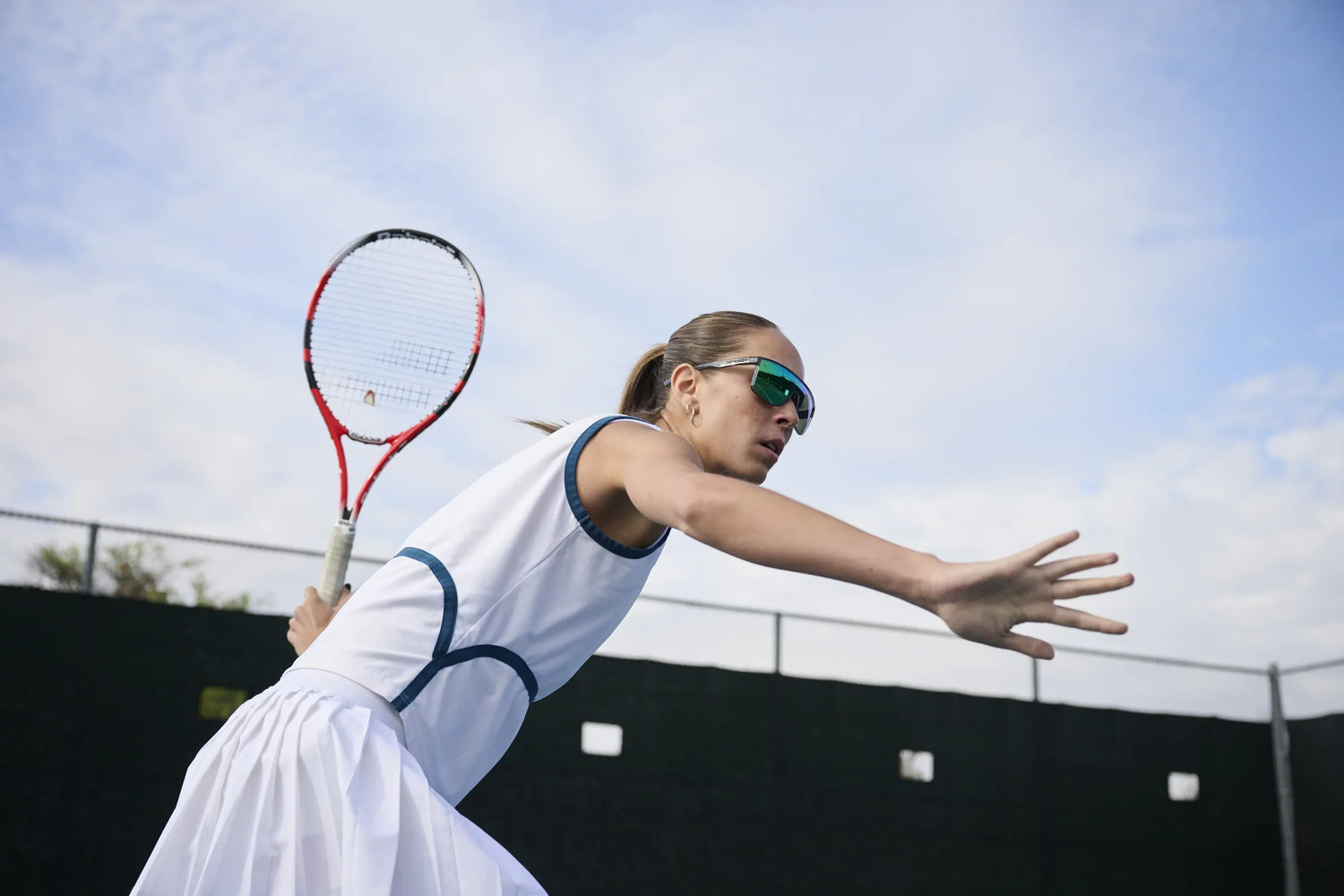 Tennis player swinging racket with tifosi sanctum sunglasses on